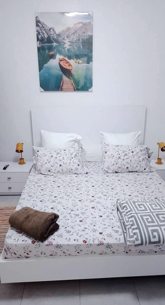 Chambre avec balcon : lit double au linge fleuri, lampes de chevet orangées et tableau d'un lac de montagne