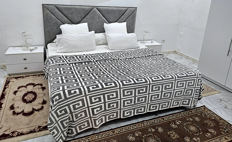 Chambre King Size : lit au couvre-lit noir et blanc à motif grec, tête de lit grise et tapis