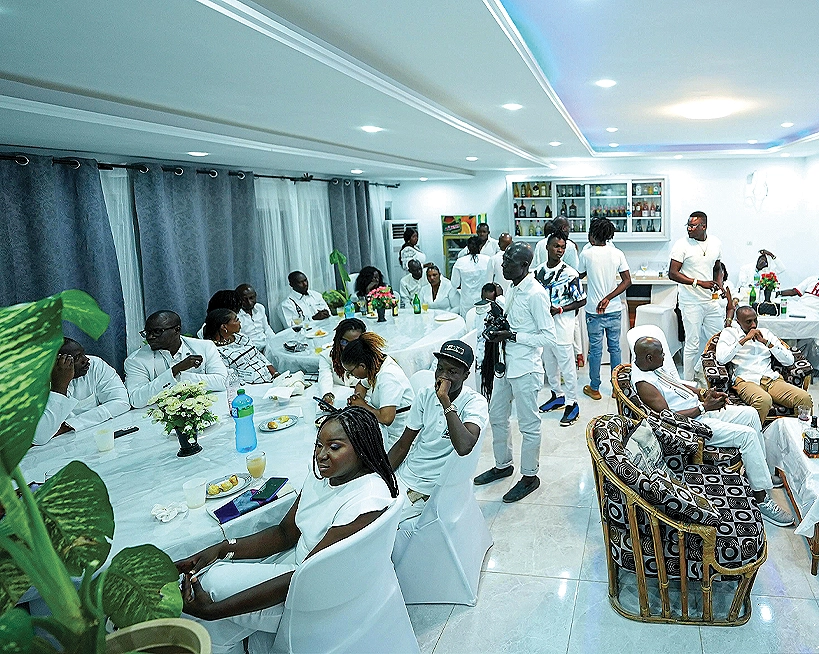 Salle de restaurant pleine d'invités vêtus de blanc autour de tables dressées