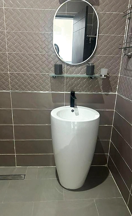 Salle de bains : vasque colonne blanche, miroir ovale et carrelage taupe